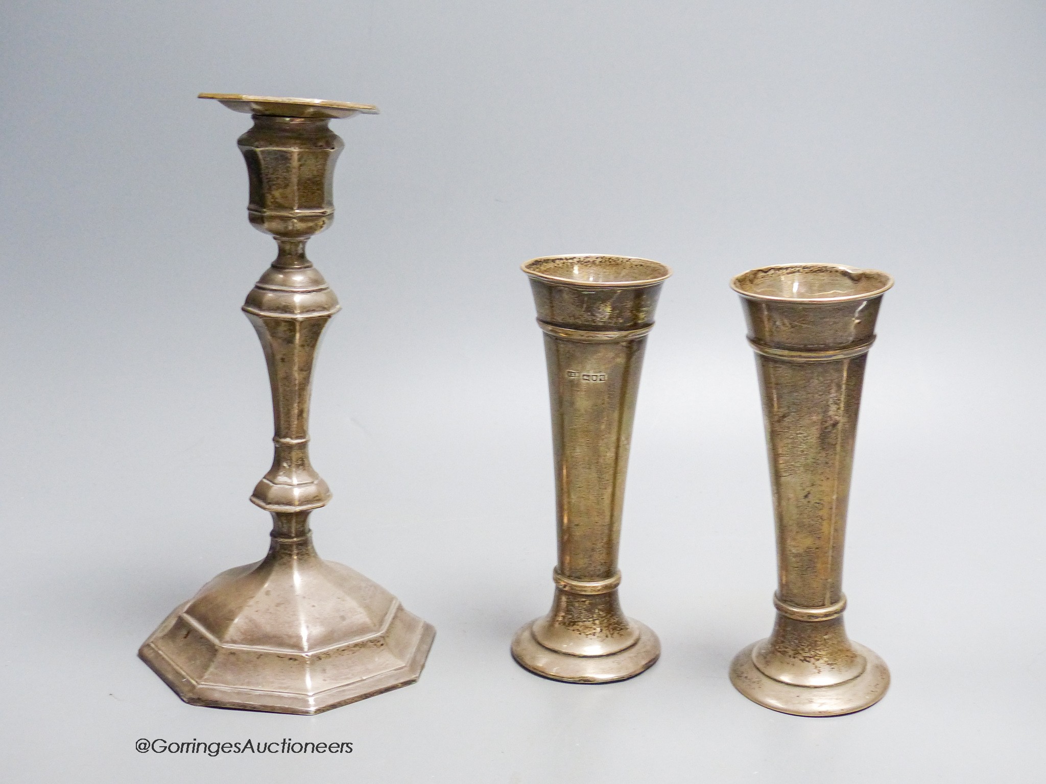 A George V silver mounted candlestick, William Hutton & Sons, Sheffield, 1912, height 20.5cm, weighted and a pair of silver posy vases, London, 1911, weighted.